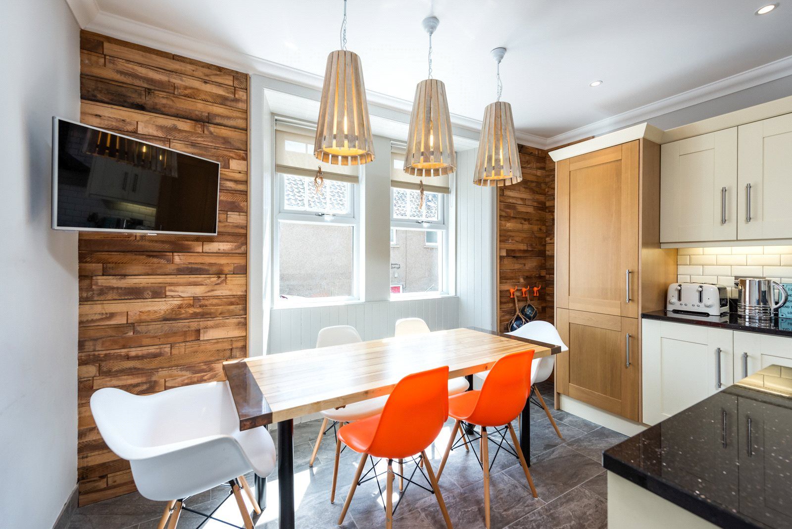 A kitchen with a large dining table, panelled walls and multicoloured chairs