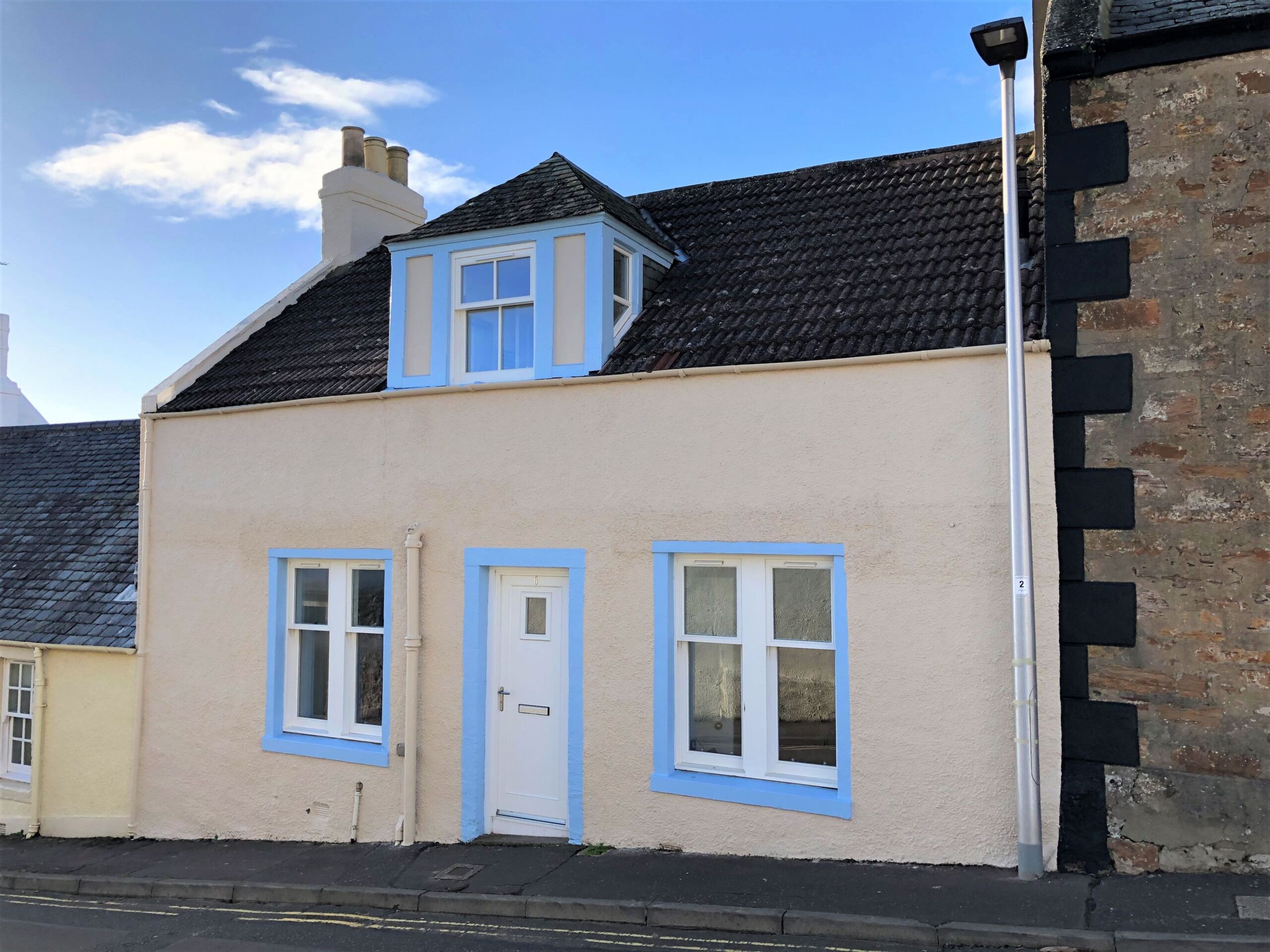 A light yellow and blue cottage on a sunny day