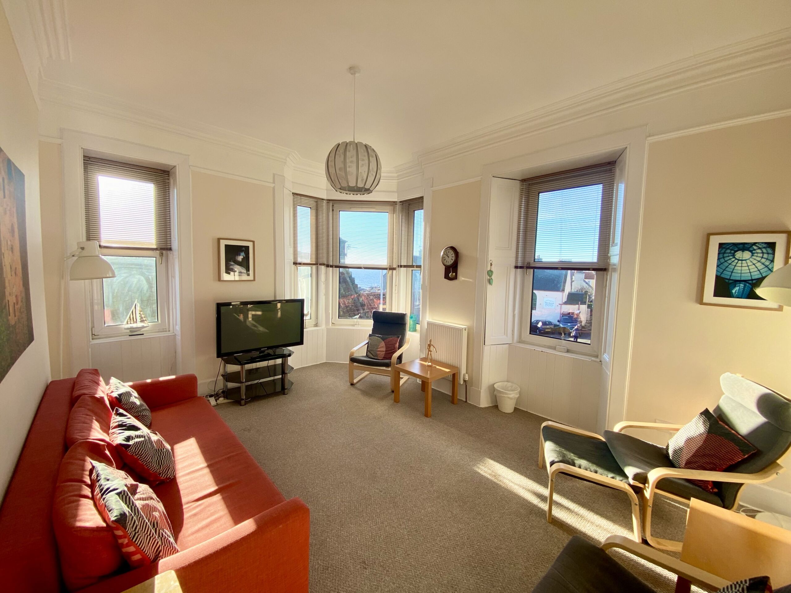 A living room with sofas, chairs, and a TV on a sunny day