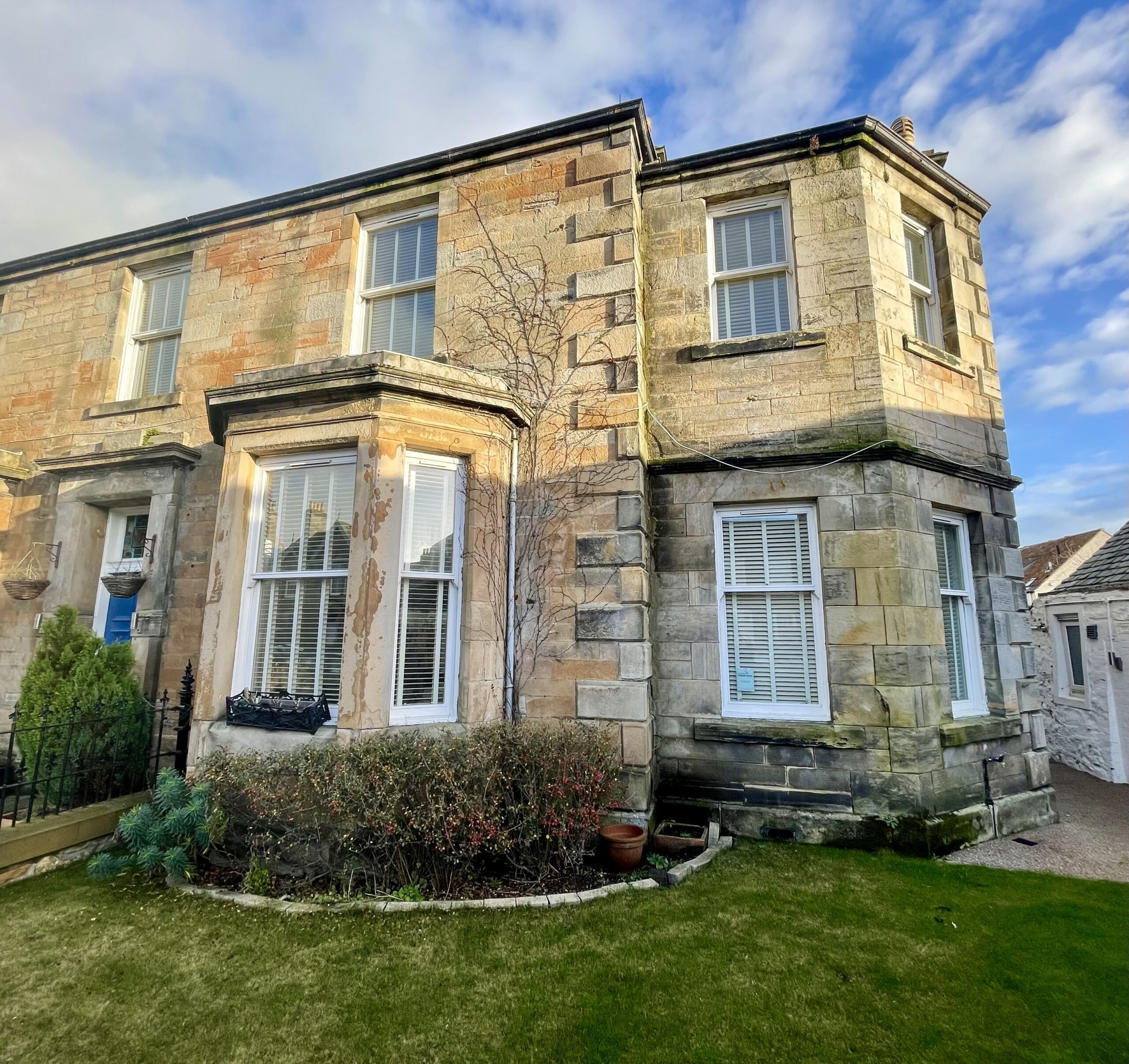 A large stone house with gardens on a sunny day