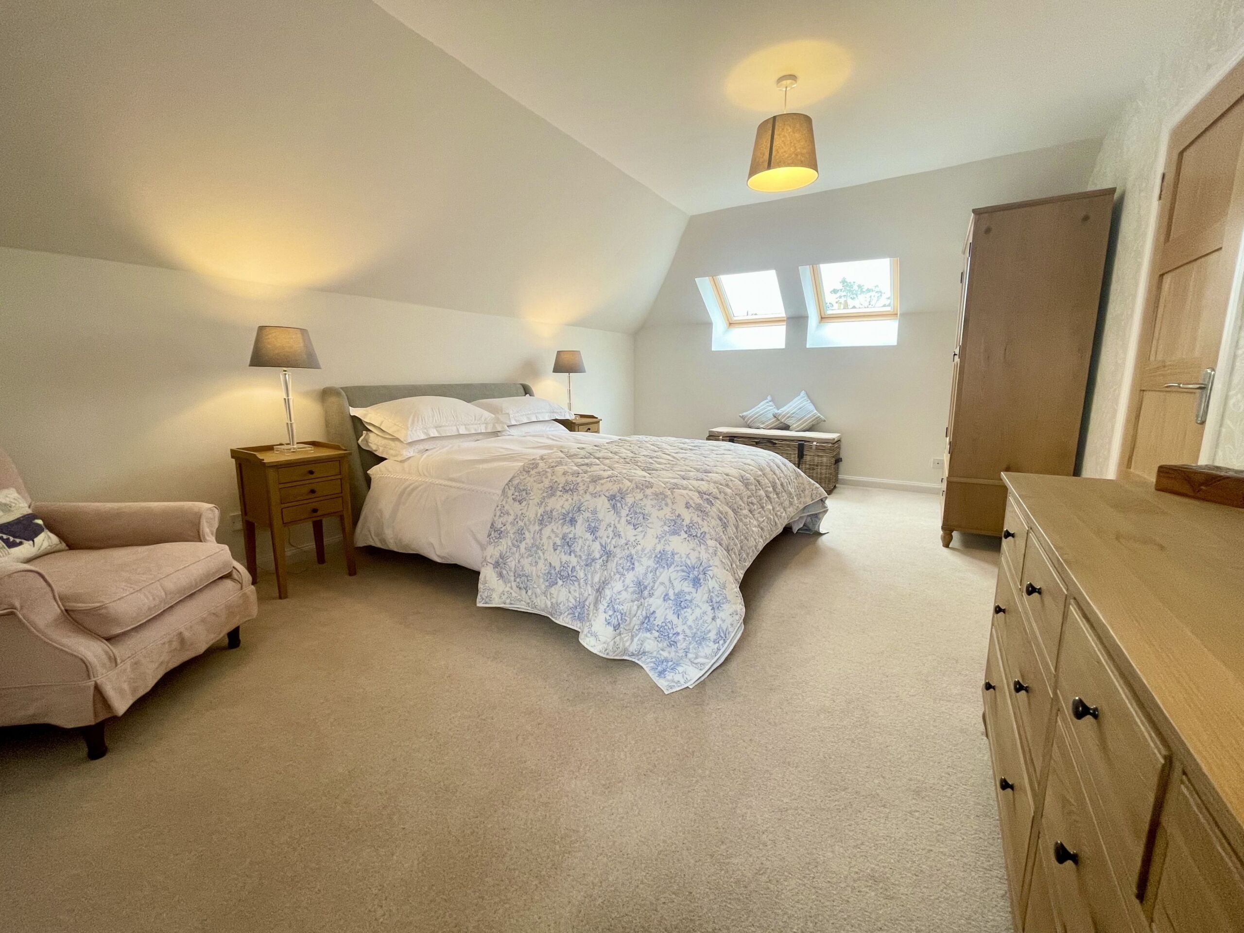 A large room with a bed, armchair and chest of drawers