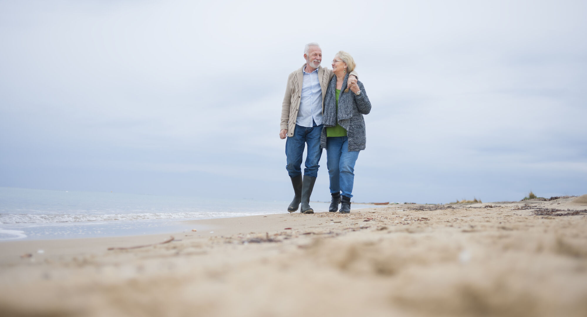 An older couple walking across a beach on a cloudy day