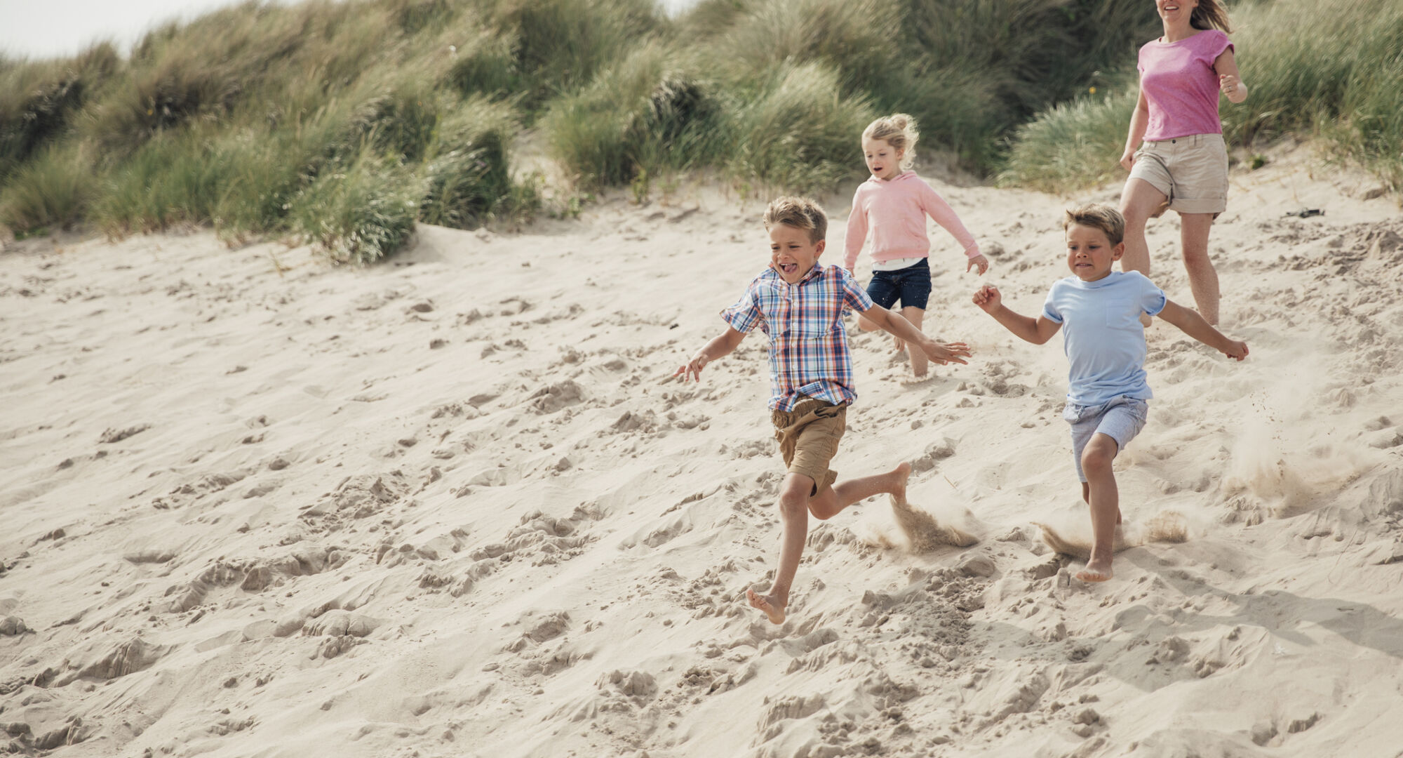 Family having fun running down the sand dunes at the beach while on holiday at the seaside