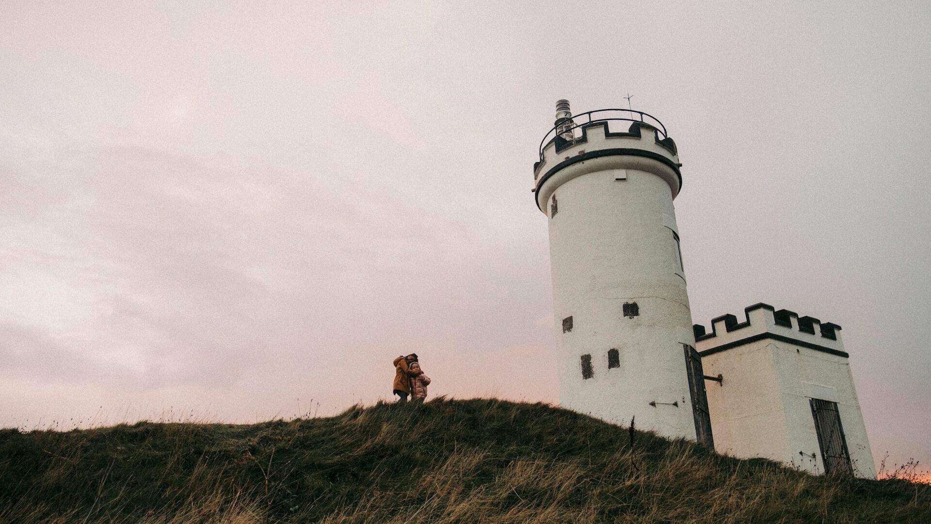 Children standing on top of a hill with a white lighthouse nearby