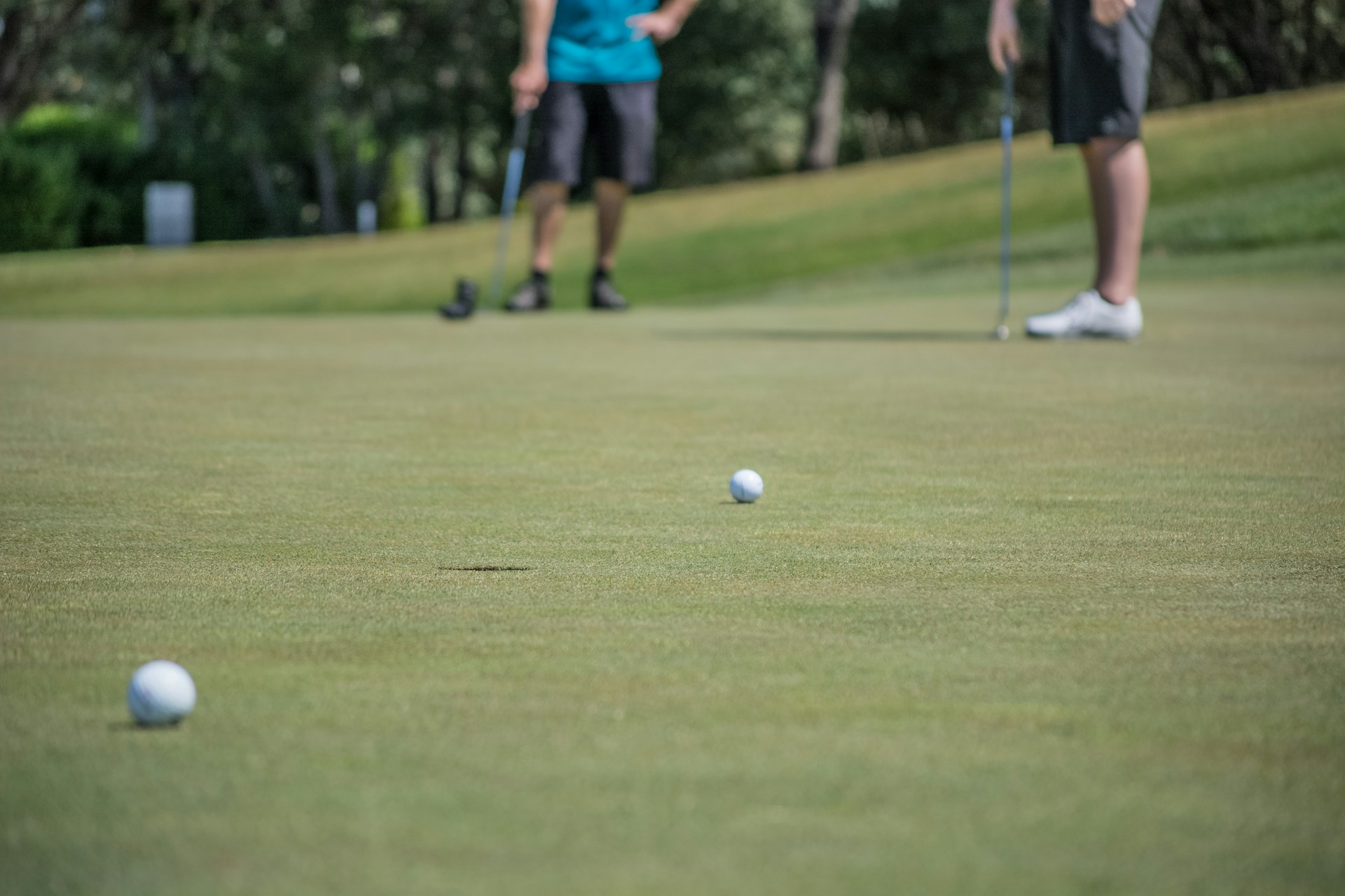 Two people stood on a golf course with balls on the floor