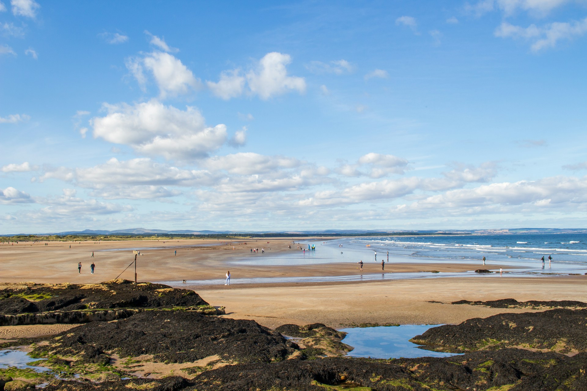 A large beach at low tide with people walking on it