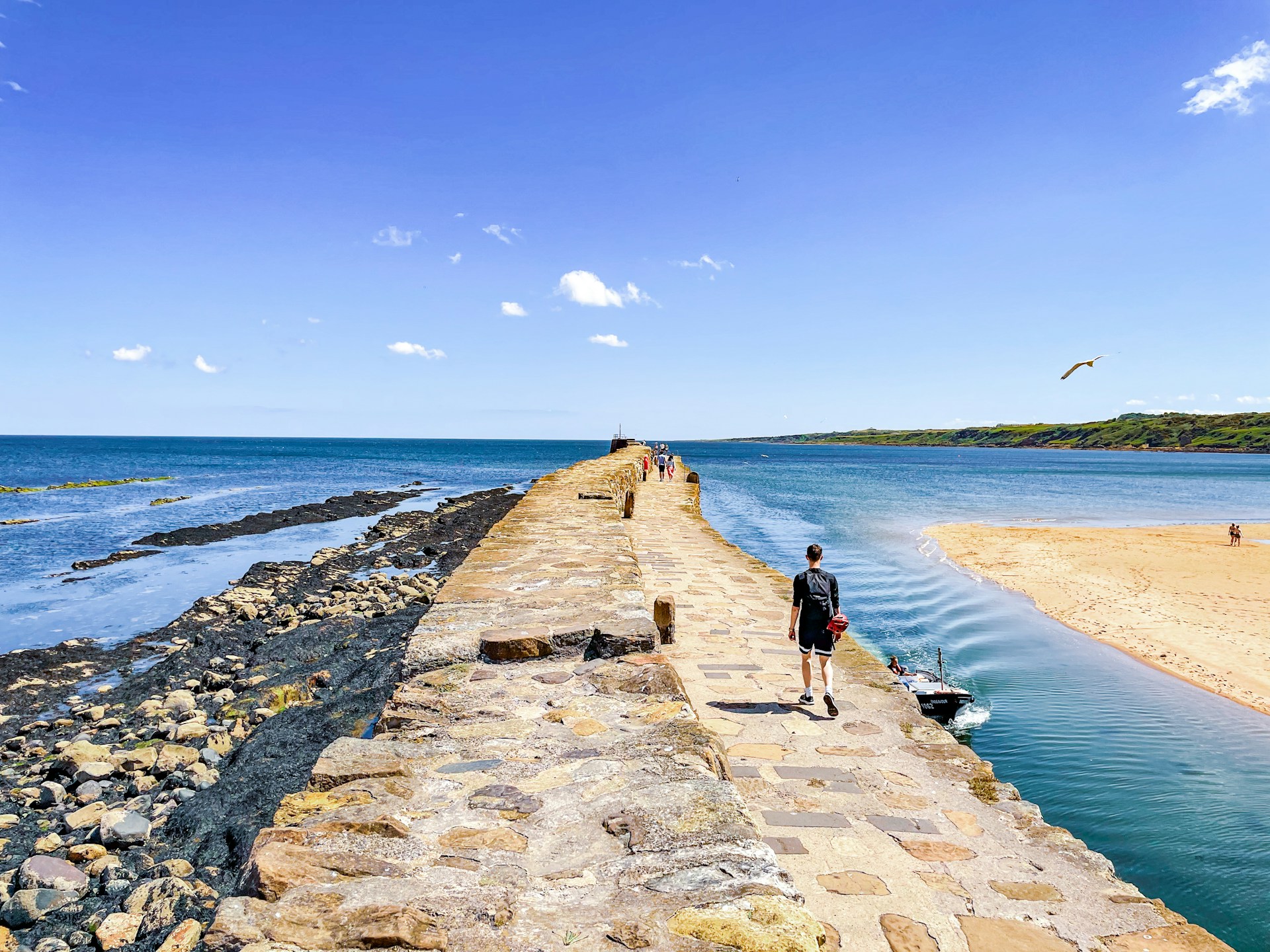 People walking out onto a stone jetty on a sunny day