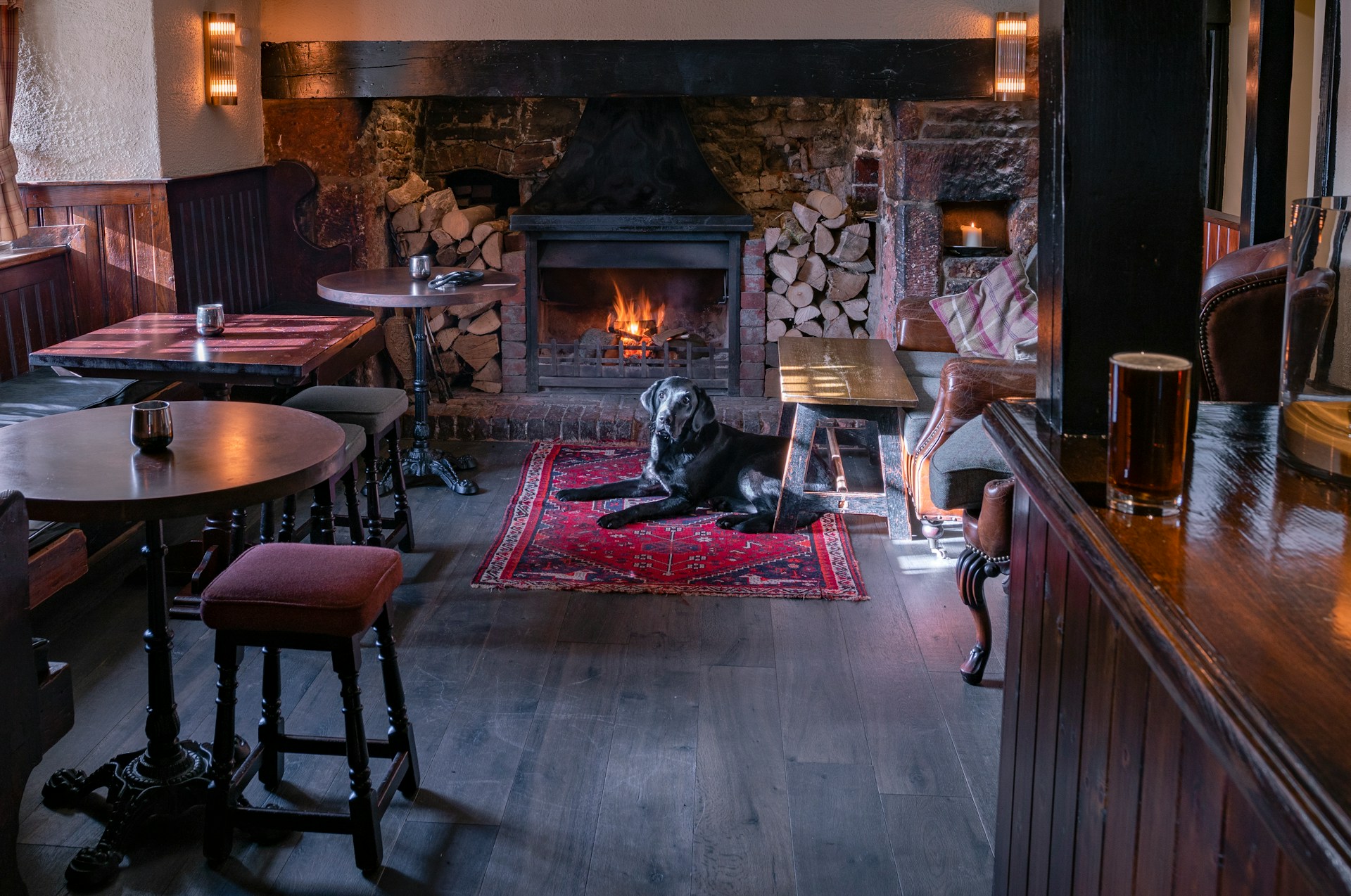 Black short coated dog lying on a rug in front of a fireplace