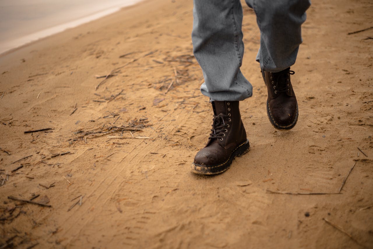 A person in jeans and and boots walking across sand