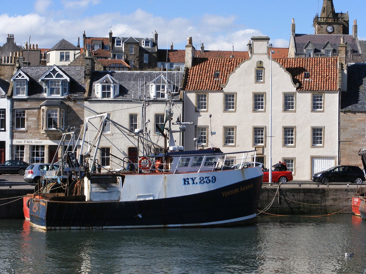 A fishing boat in a harbour overlooked by whitewashed houses