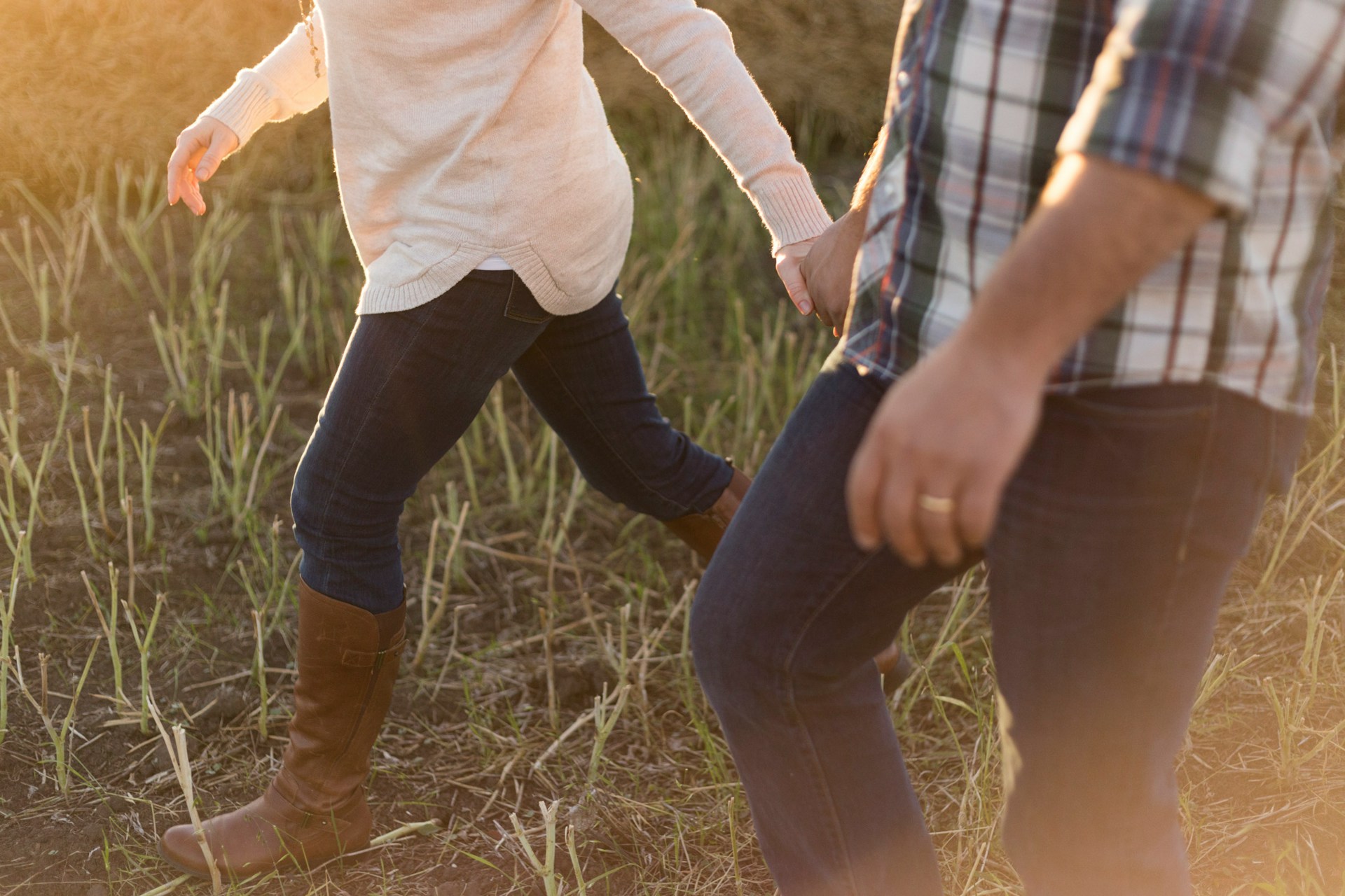 Two people holding hands walking through a grass field