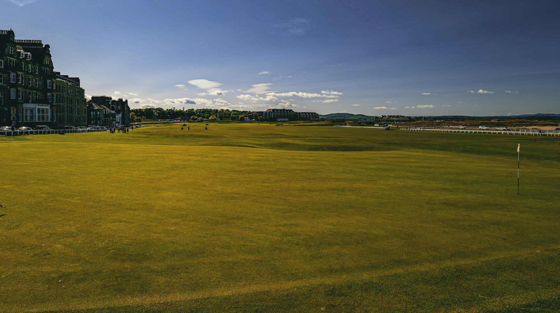 A large green golf course with buildings and trees in the distance