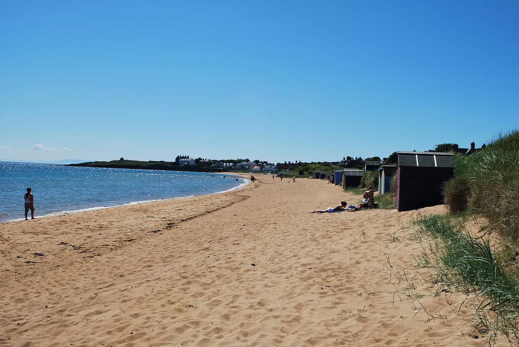 A wide sandy beach with buildings and people walking