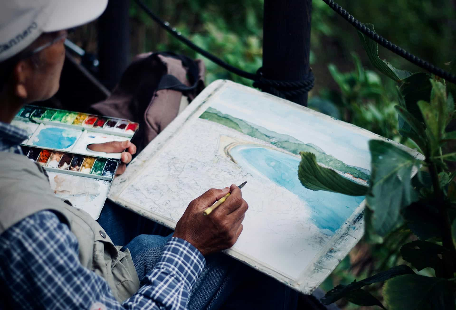 A person wearing a hat and painting with water colours