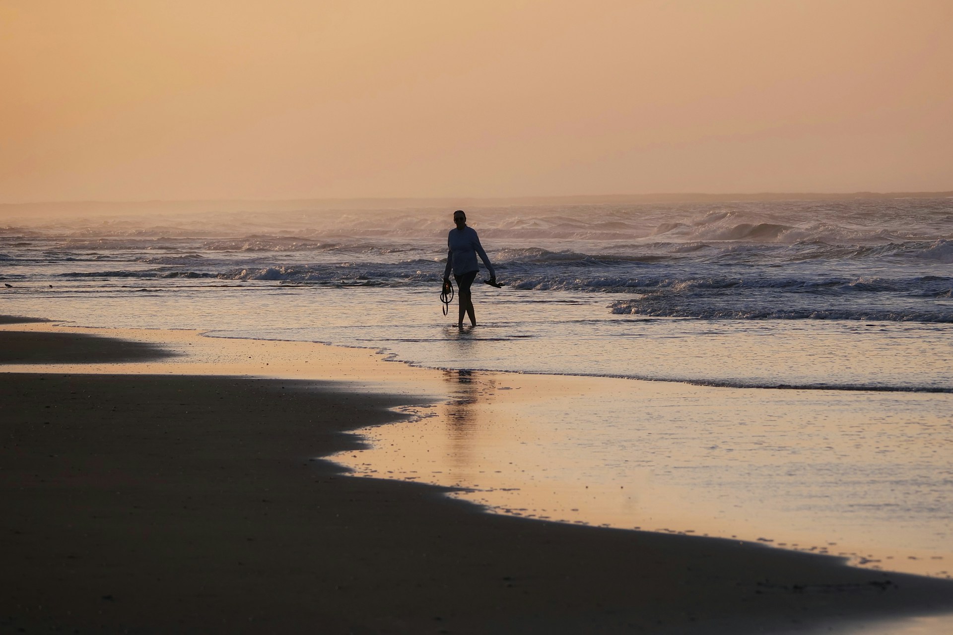 A person walking across a beach at sunset