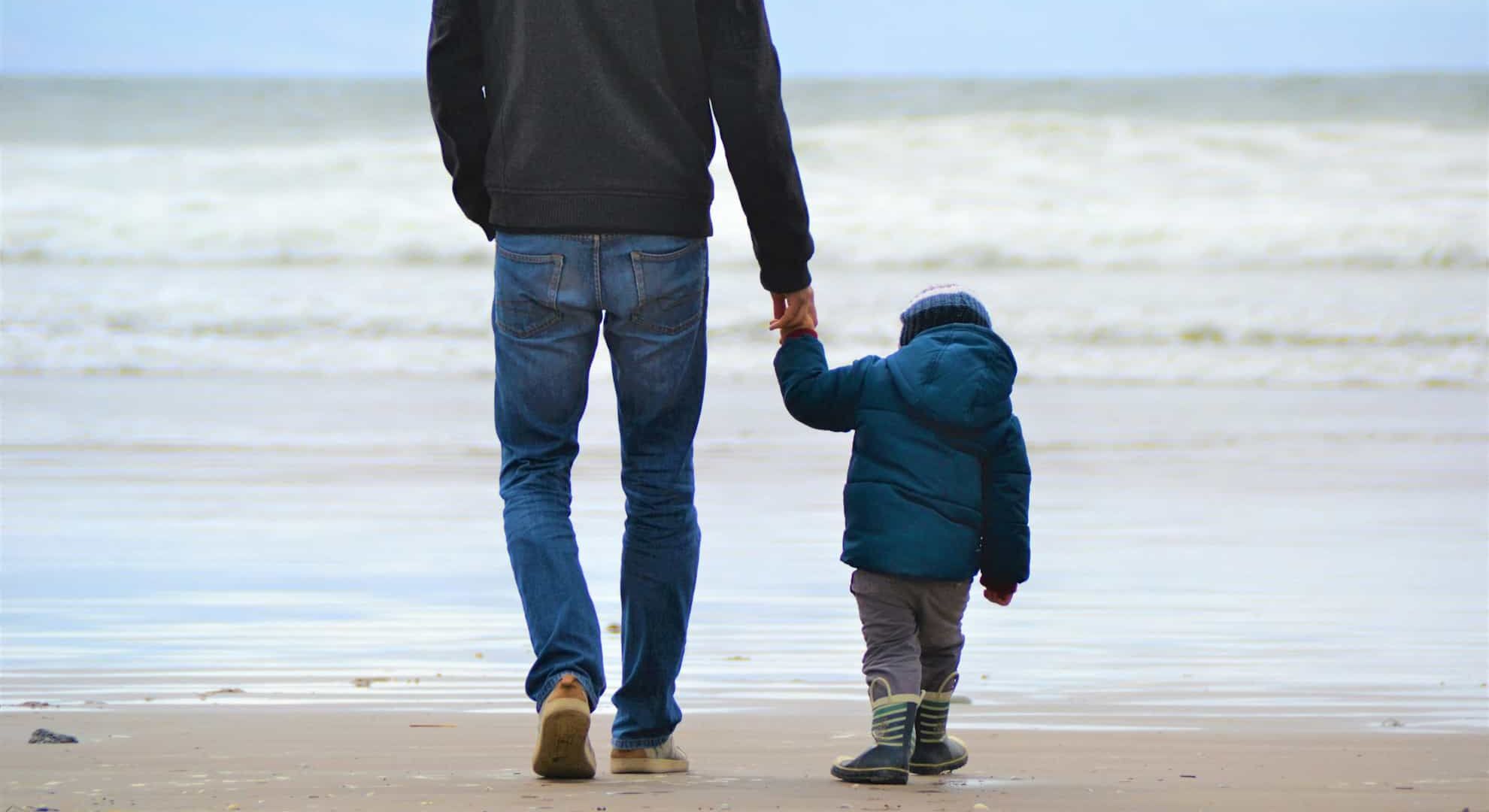 A man and a toddler walking on a beach